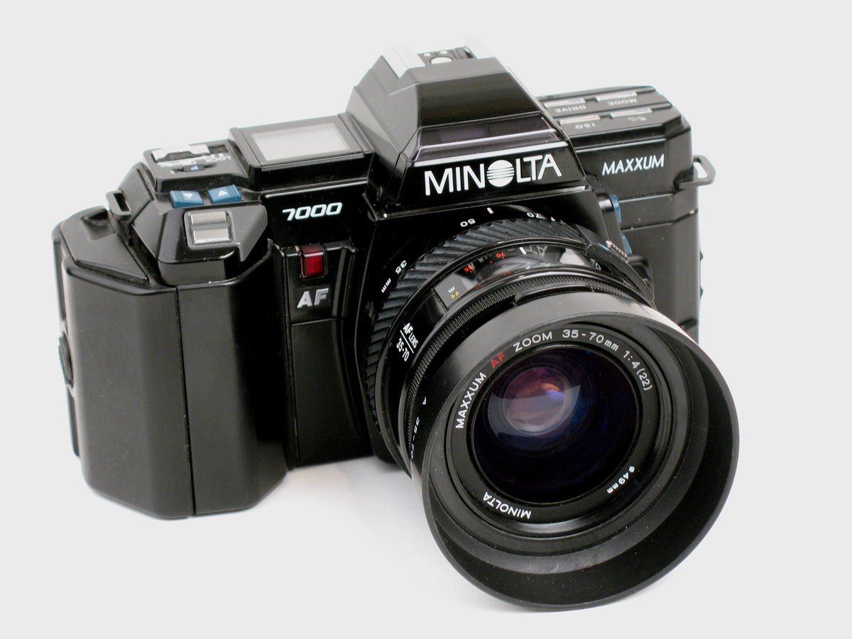 Black Minolta Maxxum 7000 SLR from 1985, seen from the front left, with the AF 35-70mm zoom lens and hood on a white background