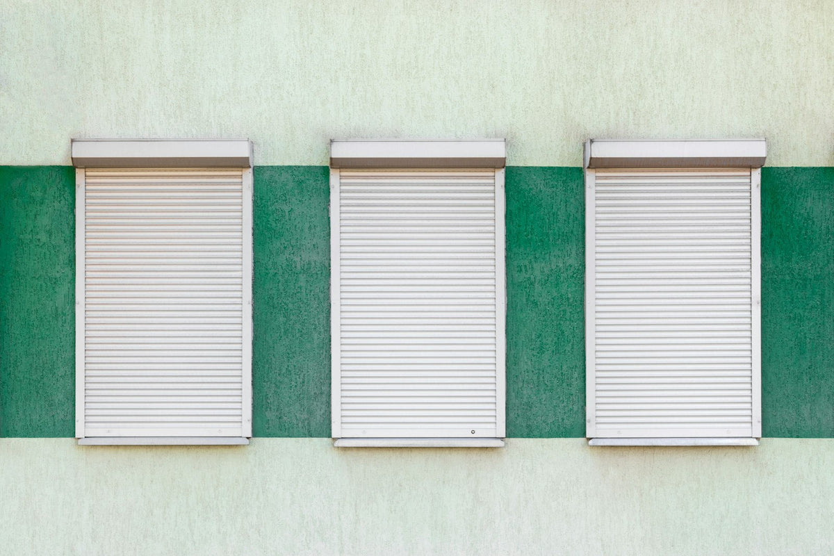 Three closed metal roller shutters in a row on a plain building front